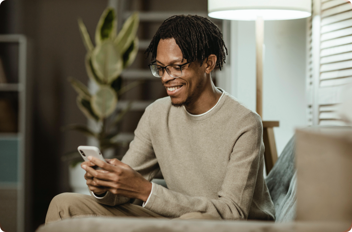 Homem negro sentado sorrindo mexendo no celular